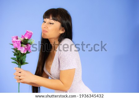 Brunette smiling young woman holding flowers over purple background.