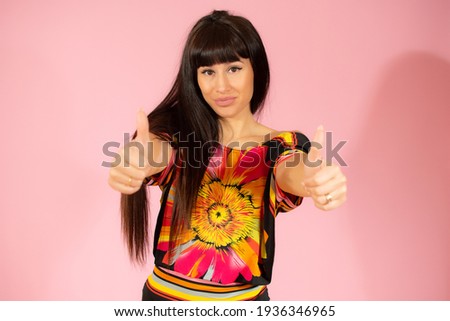 Attractive young woman giving a thumbs up gesture of approval and success over pink background.