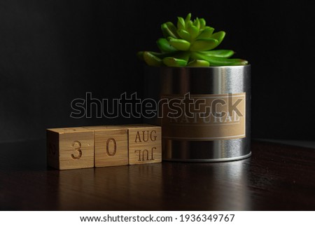 Aaugust 30. Image of the calendar August 30 wooden cubes and an artificial plant on a brown wooden table reflection and black background. with empty space for text