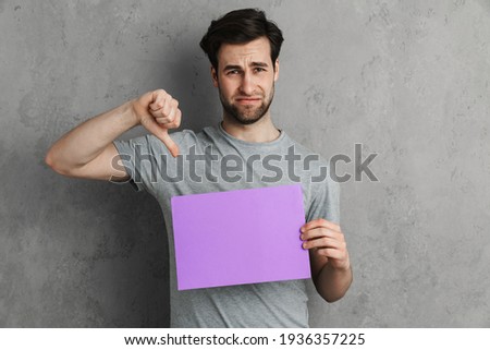 Young upset handsome man holding banner standing over isolated yellow background, negative sign showing dislike with thumbs down, rejection concept