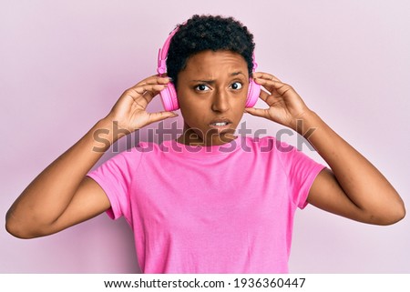Young african american girl listening to music using headphones clueless and confused expression. doubt concept. 