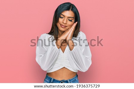 Young latin transsexual transgender woman wearing casual clothes sleeping tired dreaming and posing with hands together while smiling with closed eyes. 