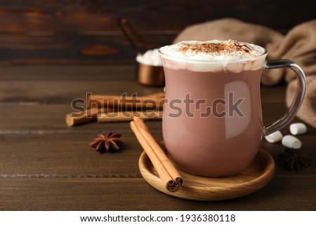 Glass cup of hot cocoa with whipped cream and aromatic cinnamon on wooden table. Space for text Royalty-Free Stock Photo #1936380118