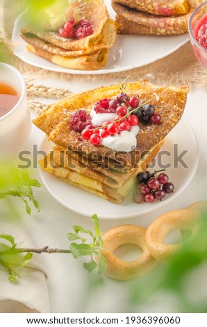 Pancakes with berries and sour cream for the Russian Maslenitsa holiday on a white background with bokeh of greens, food photo in a light key
