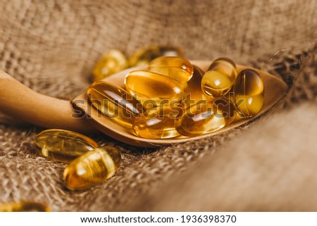 Fish oil capsules on a wooden spoon. Fish oil pills, tablets on the burlap. Vitamin complex omega 3,6,9. Fish oil capsules with omega-3, vitamin D. Close up Royalty-Free Stock Photo #1936398370