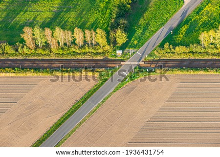 Aerial view of a processed cereal field, country road and railway crossing on a sunny autumn evening just before sunset