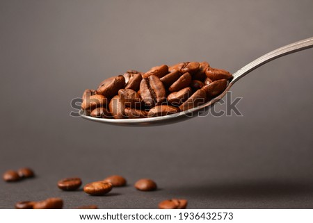 Macro shot of Selected high quality roasted coffee beans served in vintage silver table spoon on dark background with scattered coffee out of focus. Dark mood air food drink creative ads concept