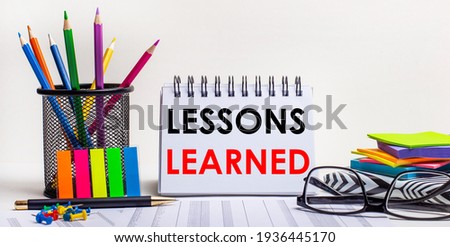 On the table are colored pencils in a stand, brightly colored stickers, glasses and a notebook with the inscription LESSONS LEARNED. Royalty-Free Stock Photo #1936445170