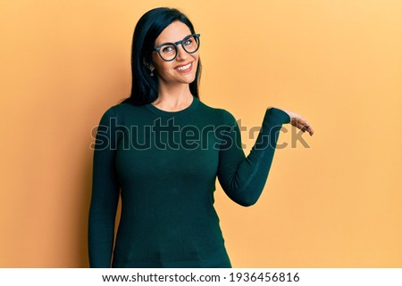 Young caucasian woman wearing casual clothes and glasses smiling cheerful presenting and pointing with palm of hand looking at the camera. 