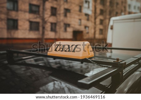 yellow taxi emblem on the roof of a car against the background of a residential apartment building
