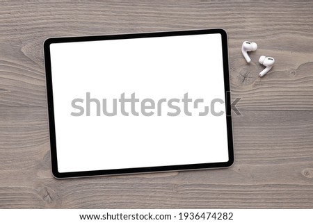 Blank white screen of tablet and wireless earphones on table