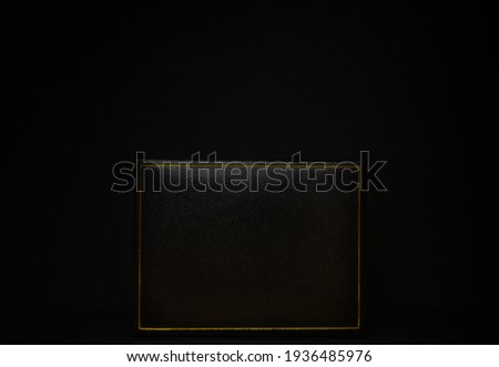 Black gift box with golden frame on black background, black on black