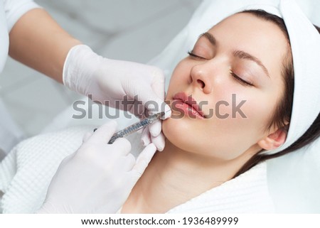 Lip augmentation and correction procedure in a cosmetology salon. The specialist makes an injection in the patient lips. Royalty-Free Stock Photo #1936489999