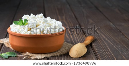 Farmer's cottage cheese in a traditional clay bowl, next to a wooden spoon, a dark wooden background. Close-up, selective focus. Soft curd natural healthy food, wholesome diet food Royalty-Free Stock Photo #1936498996
