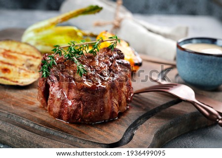 Grilled beef tenderloin steak on a wooden board with grilled vegetables. Filet Mignon recipe concept, selective focus Royalty-Free Stock Photo #1936499095