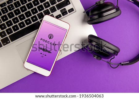 Smartphone playing a podcast. Mobile phone, laptop and headphones on violet background. Concept of listening to podcast Royalty-Free Stock Photo #1936504063