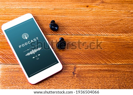 Smartphone playing a podcast. Mobile phone and earphones on wooden table. Concept of listening to podcast Royalty-Free Stock Photo #1936504066