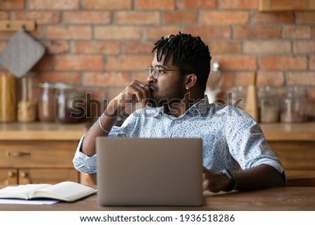 Thoughtful african male freelancer sit by laptop look aside ponder on business problem. Pensive young black man marketing expert work from home analyse sales stats plan creative concept for new brand Royalty-Free Stock Photo #1936518286