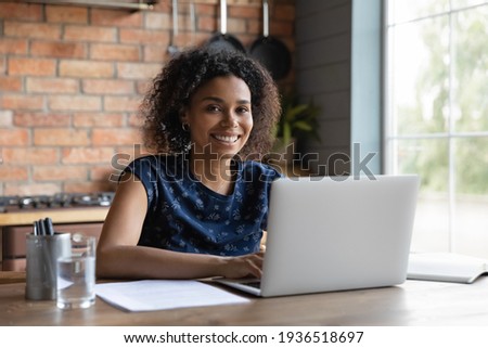 Portrait of smiling biracial female self employed freelancer at work using laptop pc doing research project. Positive motivated young black lady remote student look at camera distracted from learning