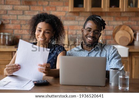 Affairs in order. Happy black family couple engaged in home accounting pay bills using laptop. Young afro american spouses check review financial papers feel satisfied glad of making payments in time Royalty-Free Stock Photo #1936520641