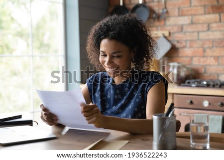 Joyful young mixed race female open paper written letter happy to read positive news from friend. Satisfied self employed black businesswoman get official answer about receiving credit loan from bank Royalty-Free Stock Photo #1936522243