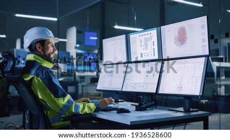 Industry 4.0 Modern Factory: Facility Operator Controls Workshop Production Line, Uses Computer with Screens Showing Complex UI of Machine Operation Processes, Controllers, Machinery Blueprints Royalty-Free Stock Photo #1936528600