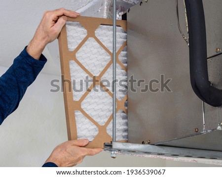 HVAC service technician changing dirty indoor air filter in residential heating and air conditioning system. Home air duct ventilation system maintenance for clean air. Royalty-Free Stock Photo #1936539067