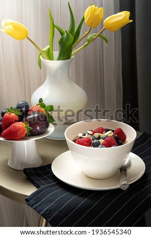 Breakfast table with tulips, bowl with porridge and berries.