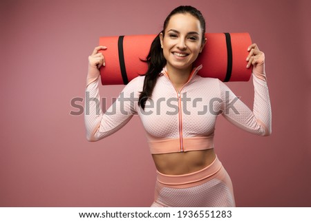 Cheerful young woman in sportswear holding yoga mat