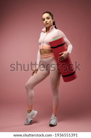 Charming young woman with yoga mat posing in studio