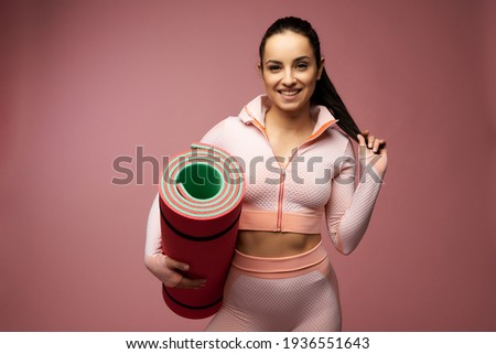 Cheerful young woman with yoga mat posing in studio