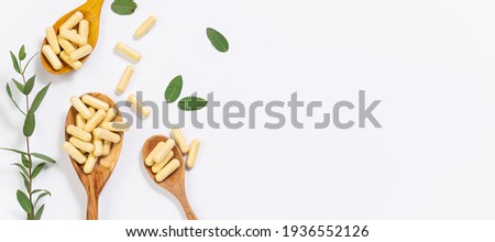 Wooden spoons with vegan vitamin capsules for immunity support and healthy lifestyle on white background with fresh green eucalyptus twig. Long banner format. Royalty-Free Stock Photo #1936552126