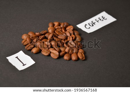 Macrophotographie shot of Love heart shape of high quality roasted arabica coffee beans on dark background, white paper sheets with I love coffee text. Copy space image
