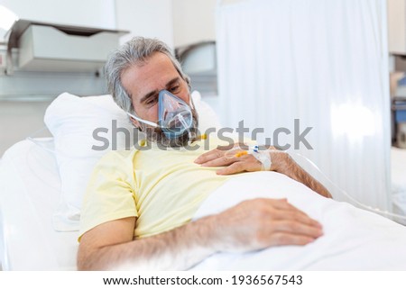 Portrait of retired senior man breathing slowly with oxygen mask during coronavirus covid-19 outbreak. Old sick man lying in hospital bed, getting treatment for deadly infection Royalty-Free Stock Photo #1936567543