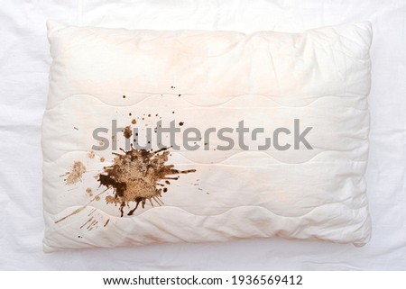 Old used white pillow with stains on crumpled sheet, dirty pillow on the bed