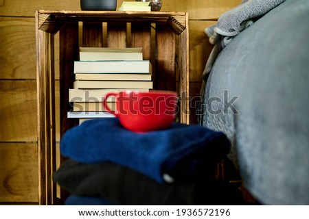 Books on the shelf with pile of clothes and red cup