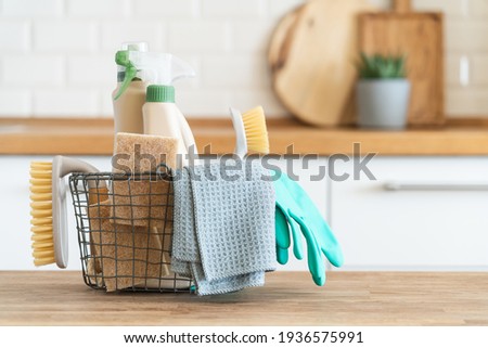 Basket with brushes, rags, natural sponges and cleaning products. Modern kitchen interior in the background. House cleaning concept Royalty-Free Stock Photo #1936575991