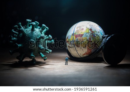 Corona virus global pandemic concept. Miniature man standing near big Corona virus novel in dark. Creative decoration with fog and backlight. Selective focus Royalty-Free Stock Photo #1936591261