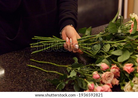 Florist works with colors. Flower seller chooses flowers for future bouquet. Flowers shop worker in a mask standing in flower shop and checking flowers in glass vase.