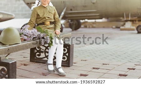 Girl in a military uniform of a Soviet soldier with a bouquet of lilacs on the background of an airplane. Concept cards for the Victory Day
