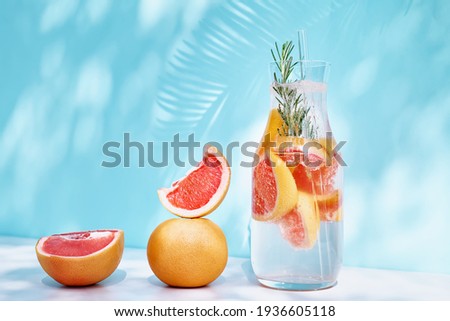 Summer cocktail with grapefruit and rosemary and juicy slices citrus fruits. Fresh healthy grapefruit beverage on sunlight with shadows. Creative drink on blue pastel background. Royalty-Free Stock Photo #1936605118