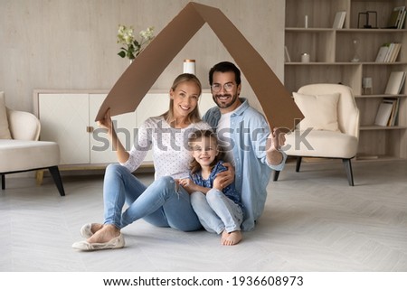 Portrait of happy young Caucasian family with daughter relax under roof celebrate relocation to own home. Smiling parents with girl child enjoy new house or apartment. Rental, real estate concept. Royalty-Free Stock Photo #1936608973