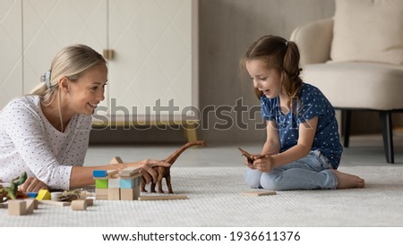 Cute little 7s girl child sit on floor play with loving young Caucasian mother enjoy family leisure weekend. Caring mom and small daughter engaged in playful activity with animal toys together. Royalty-Free Stock Photo #1936611376