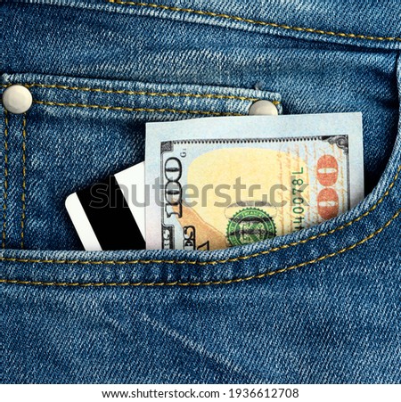 paper american dollars and plastic bank card with magnetic stripe in the pocket of blue jeans, close up