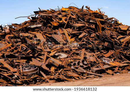 The photo shows a large, rusty pile of scrap metal in the sun