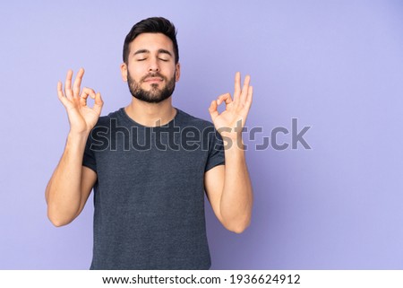 Caucasian handsome man in zen pose over isolated purple background