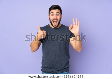 Caucasian handsome man showing ok sign and thumb up gesture over isolated purple background