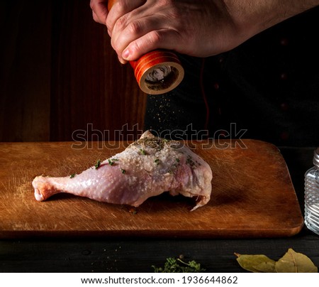 Cooking a chicken leg with the hands of a chef on a dark background. Add pepper to chicken meat. Free advertising space for restaurant
