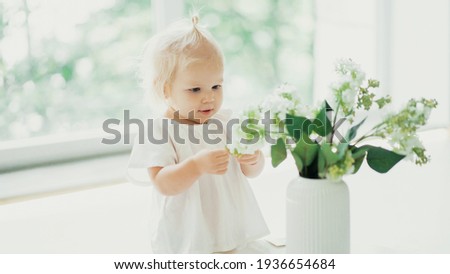 Portrait of a cute little girl with blonde blue eyes. The family spends time at home on the couch. A child plays with flowers at home alone. Children and home. A cheerful mood.