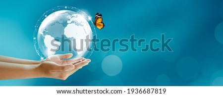 Human holding earth and butterfly over green blur background. World Environment and Green concept. Copy space. Royalty-Free Stock Photo #1936687819